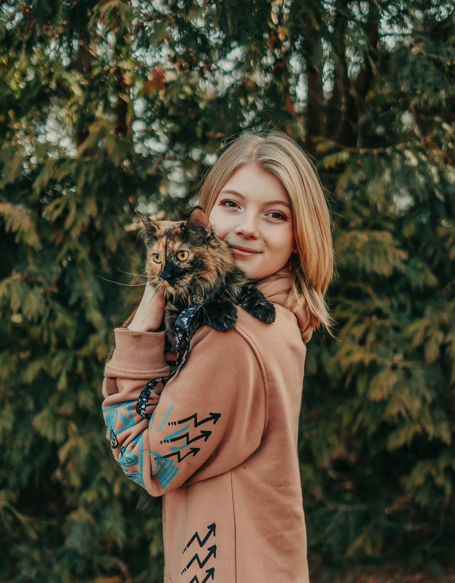 A person wearing a tan sweater poses playfully with a small black puppy outdoors.