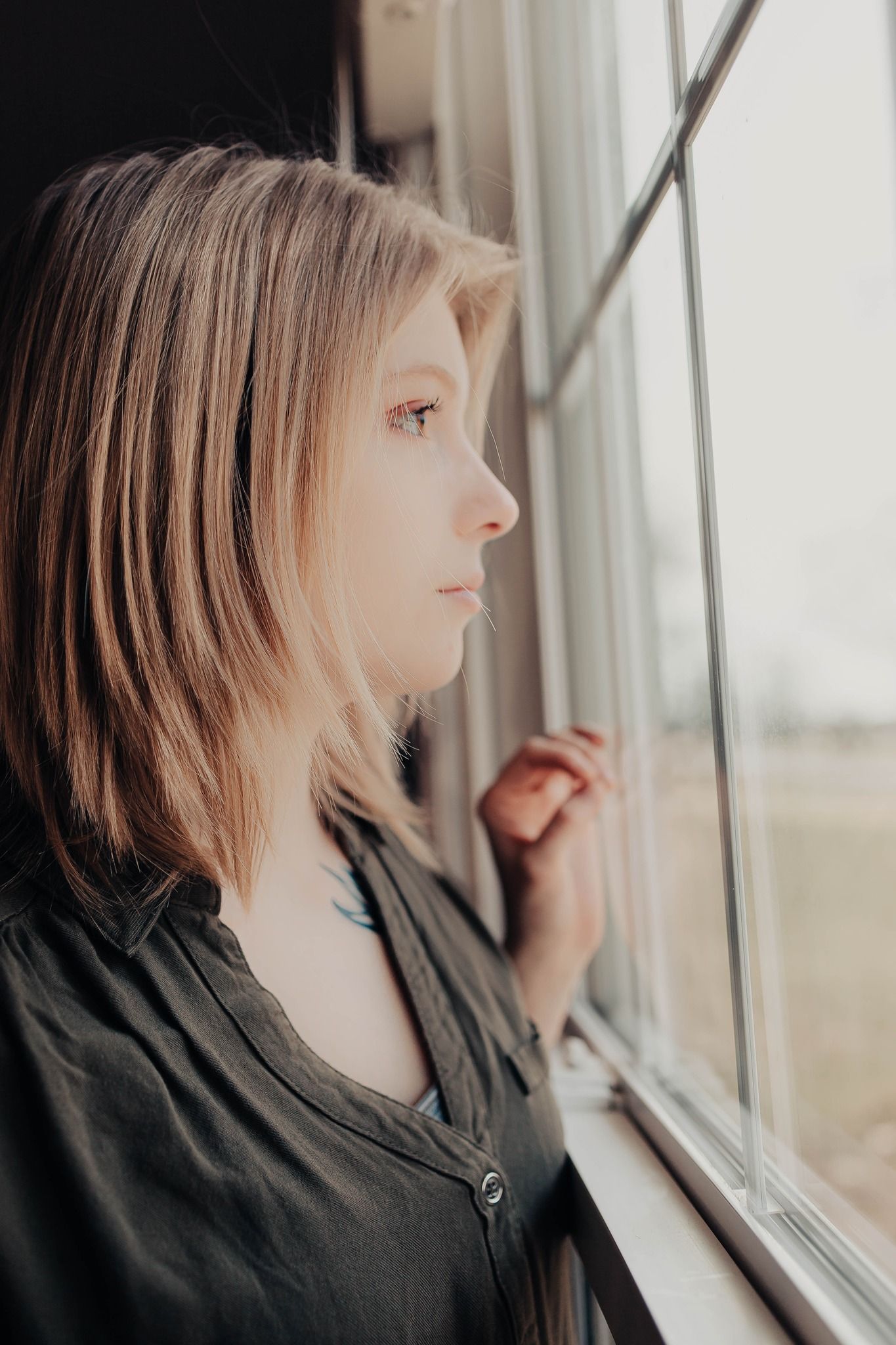A contemplative profile view of someone gazing out a window with soft natural lighting.