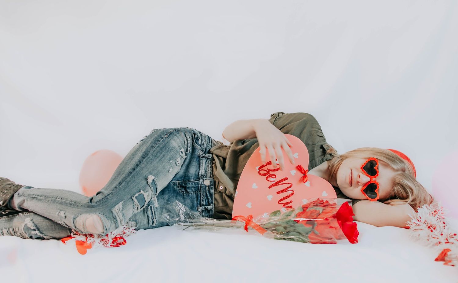 Artistic photo series showing someone lying down with red valentine decorations against white backdrop.