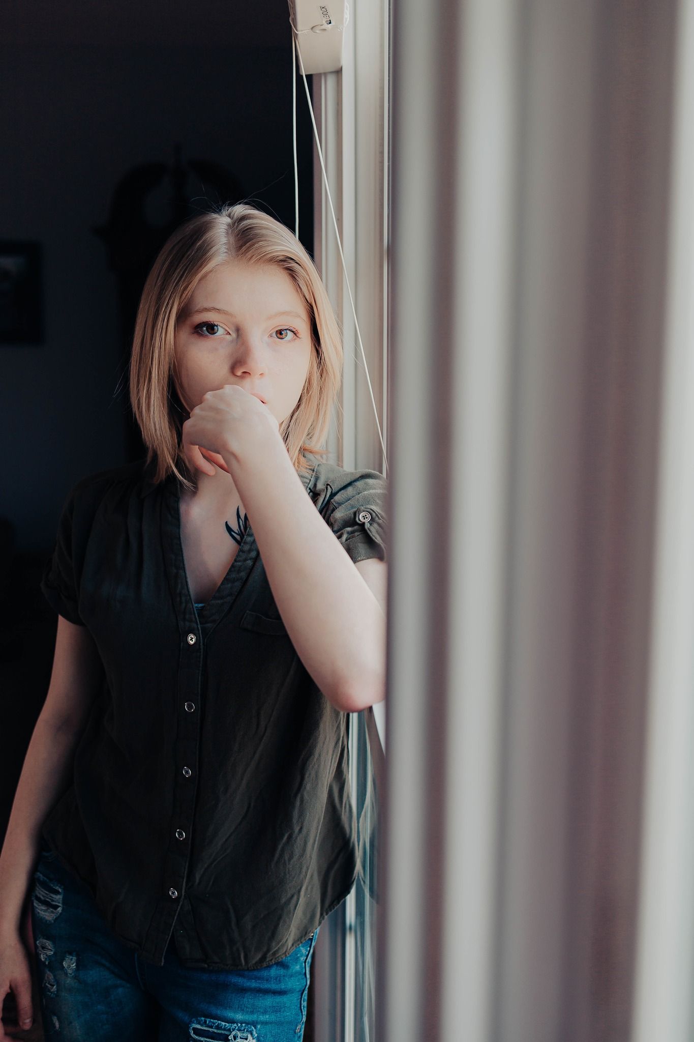 Figure in a black shirt looking contemplative by a window with natural light.