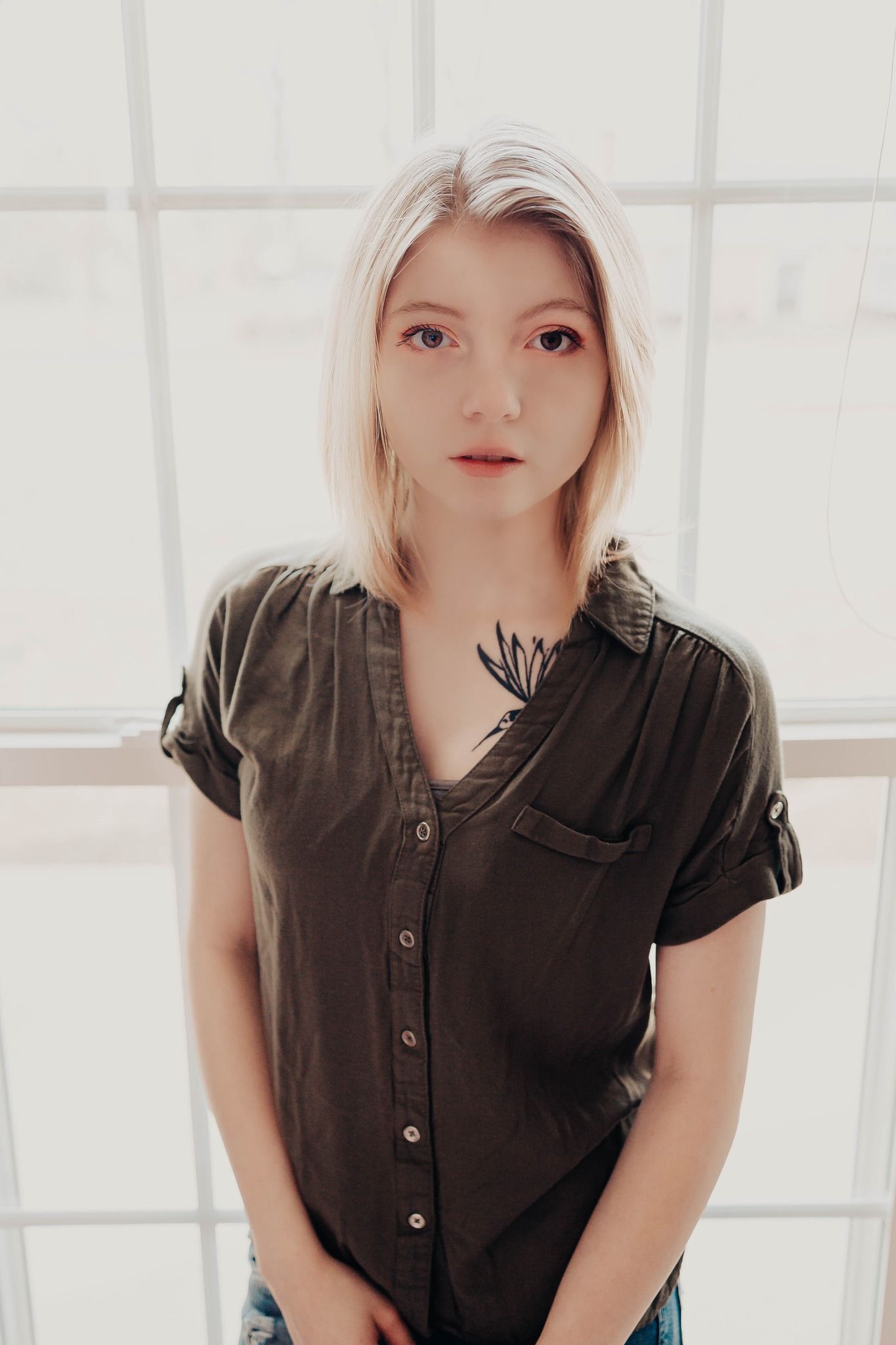 Studio portrait featuring olive button-up shirt against white tiled wall.