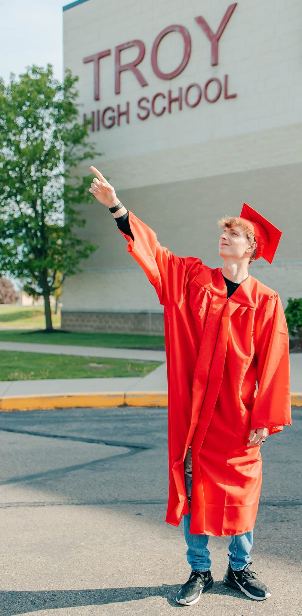 Graduate in bright red cap and gown celebrating outside Troy High School.