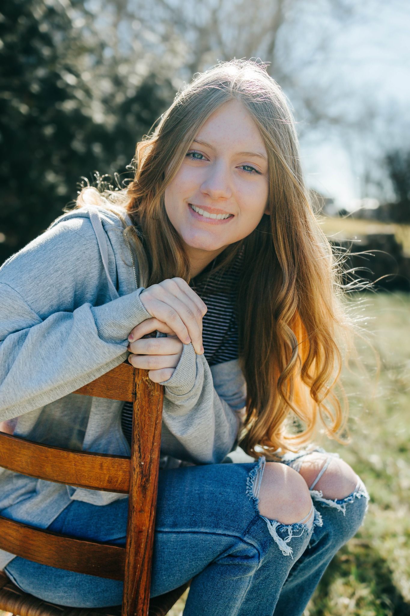 Casual outdoor portrait in denim and gray sweater sitting on wooden furniture.