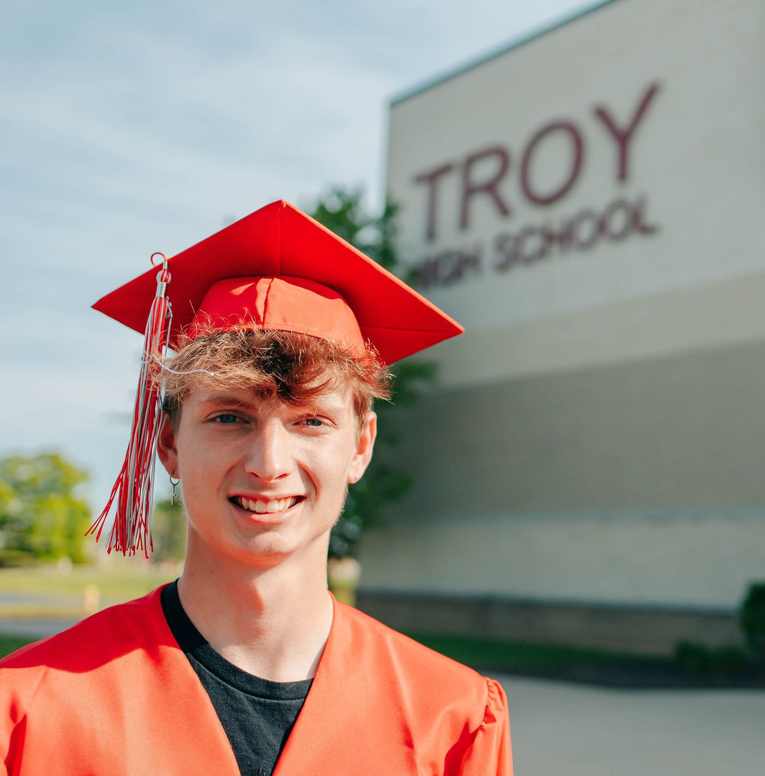 Senior photos of graduate in red cap and gown in front of Troy High School building.