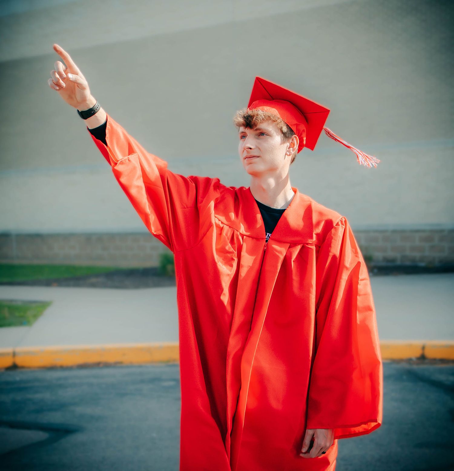 Graduate in bright red graduation gown posing against grey background.