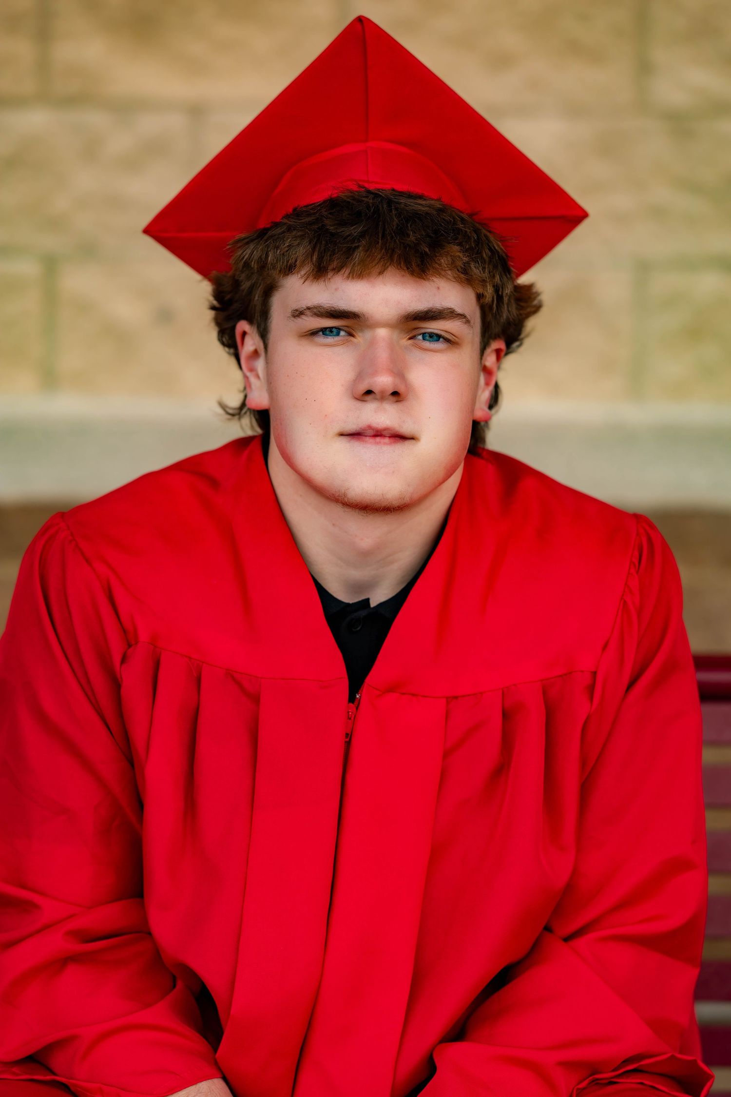 Graduate in bright red cap and gown poses for formal graduation portrait.