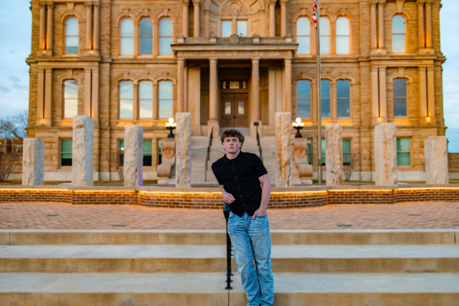 Someone stands on the steps of a grand historic building with ornate yellow sandstone architecture and tall windows.