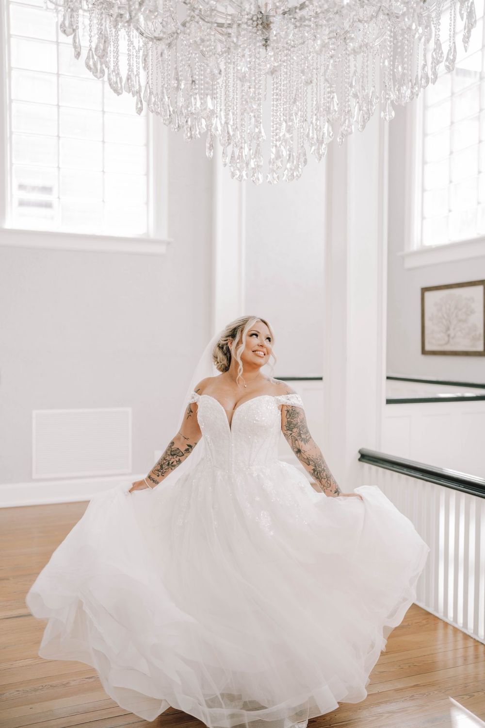 A flowing white wedding dress twirls gracefully in a bright sunlit room with hardwood floors and white walls.