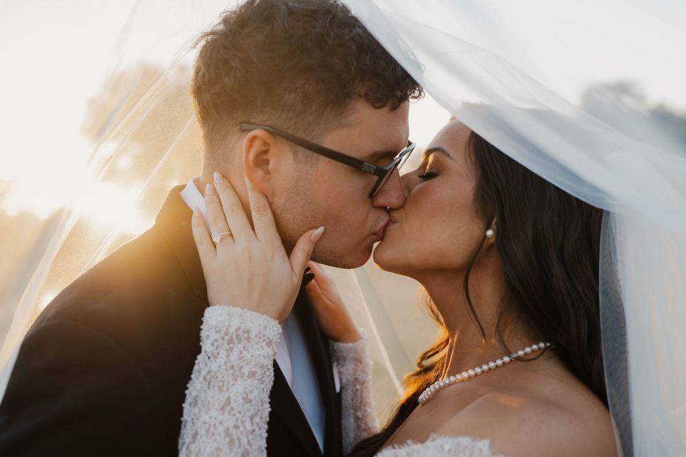 A romantic wedding couple shares tender kisses in a series of soft-lit portraits with sunlight glowing behind them.