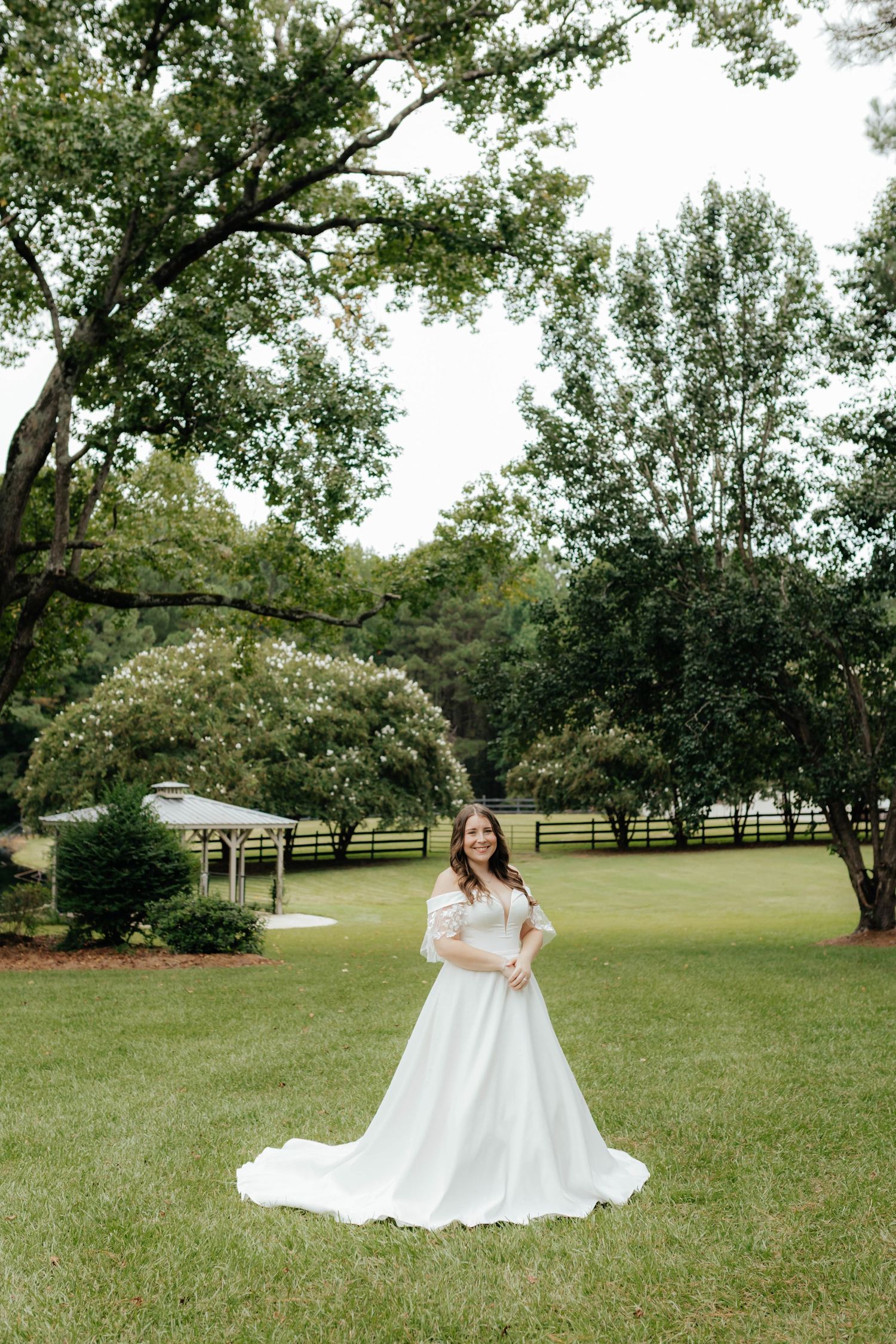 Bride in flowing white gown twirls in sunny garden setting during wedding photoshoot.