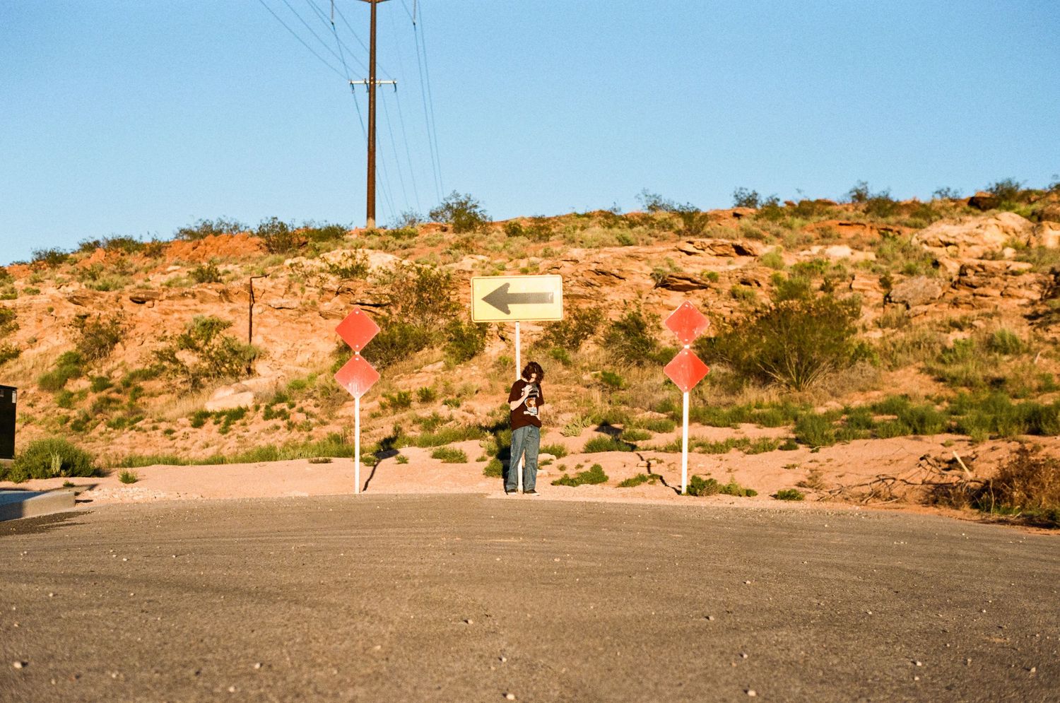 A panoramic desert landscape with utility poles stretching across the horizon and orange sandy terrain under blue sky.