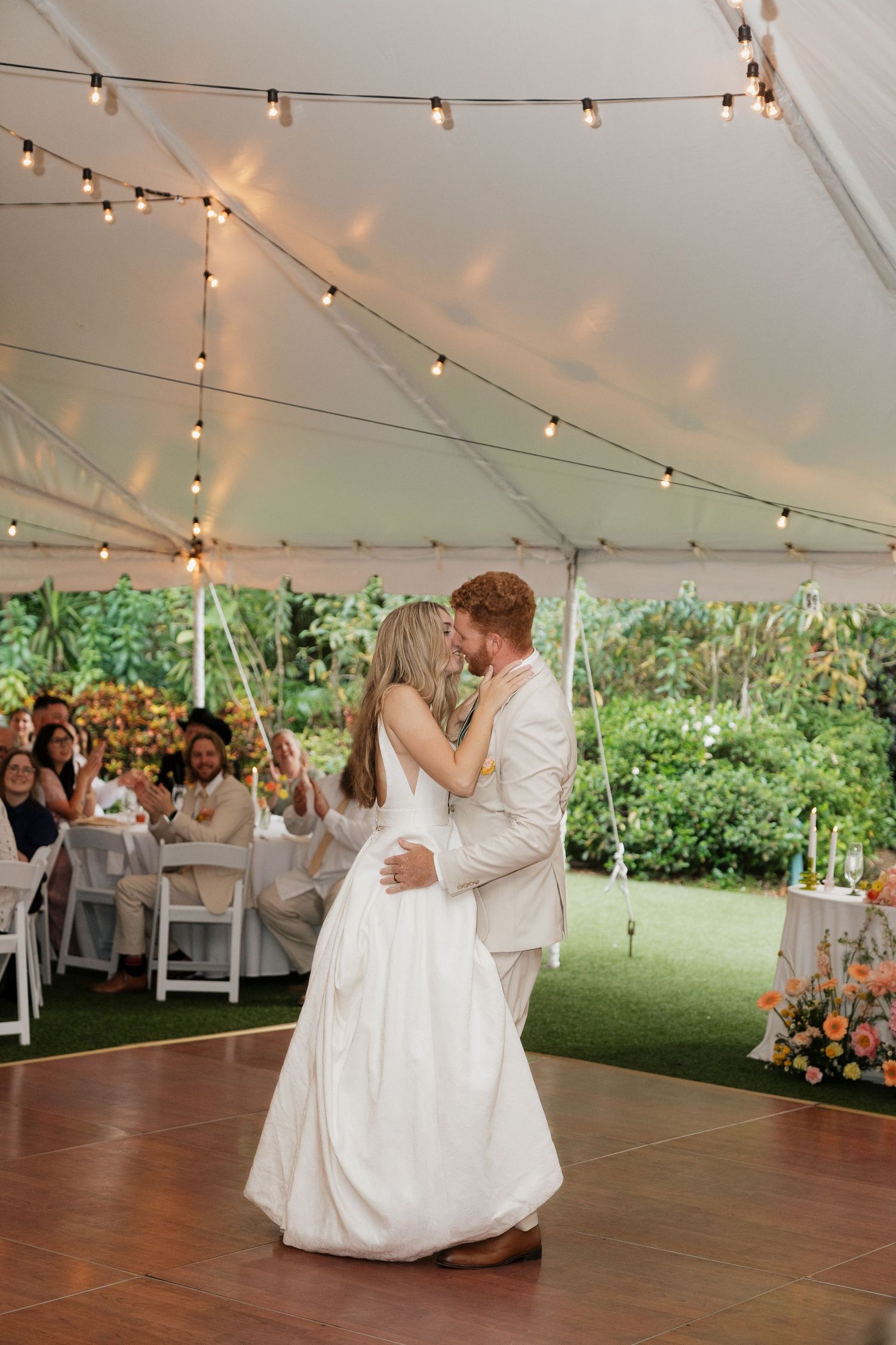 Newlyweds share their first dance under twinkling string lights in an elegant outdoor wedding tent reception.