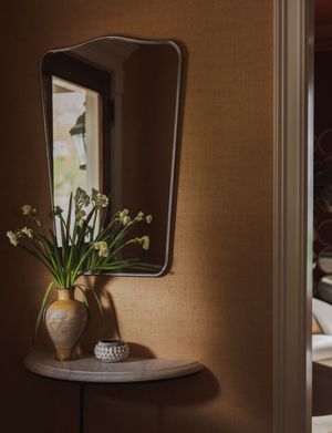 A clay vase with white flowers sits on a wooden shelf against a brown wall with dramatic lighting and shadows.