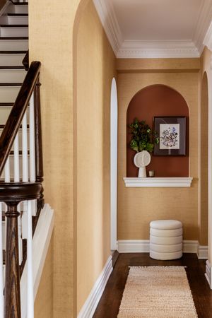 Elegant hallway with cream walls, white crown molding, dark wood stairs, and arched doorway showcasing traditional design elements.
