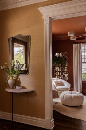 Modern interior design featuring a curved mirror, vase with flowers, and white seating visible through an elegant doorway.