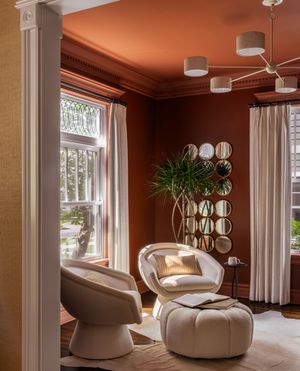 Modern living room with curved cream seating and warm terracotta walls features circular mirrors and large windows.