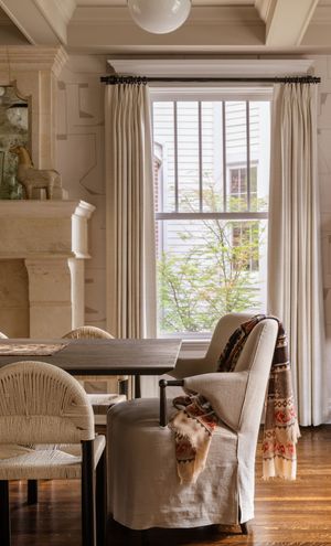 Elegant dining area with cream upholstered chairs, dark wood table, and white curtained windows in natural light.