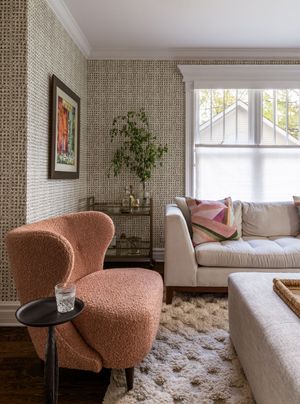 Cozy living room corner with pink upholstered chair, window seat, and textured area rug in neutral tones.