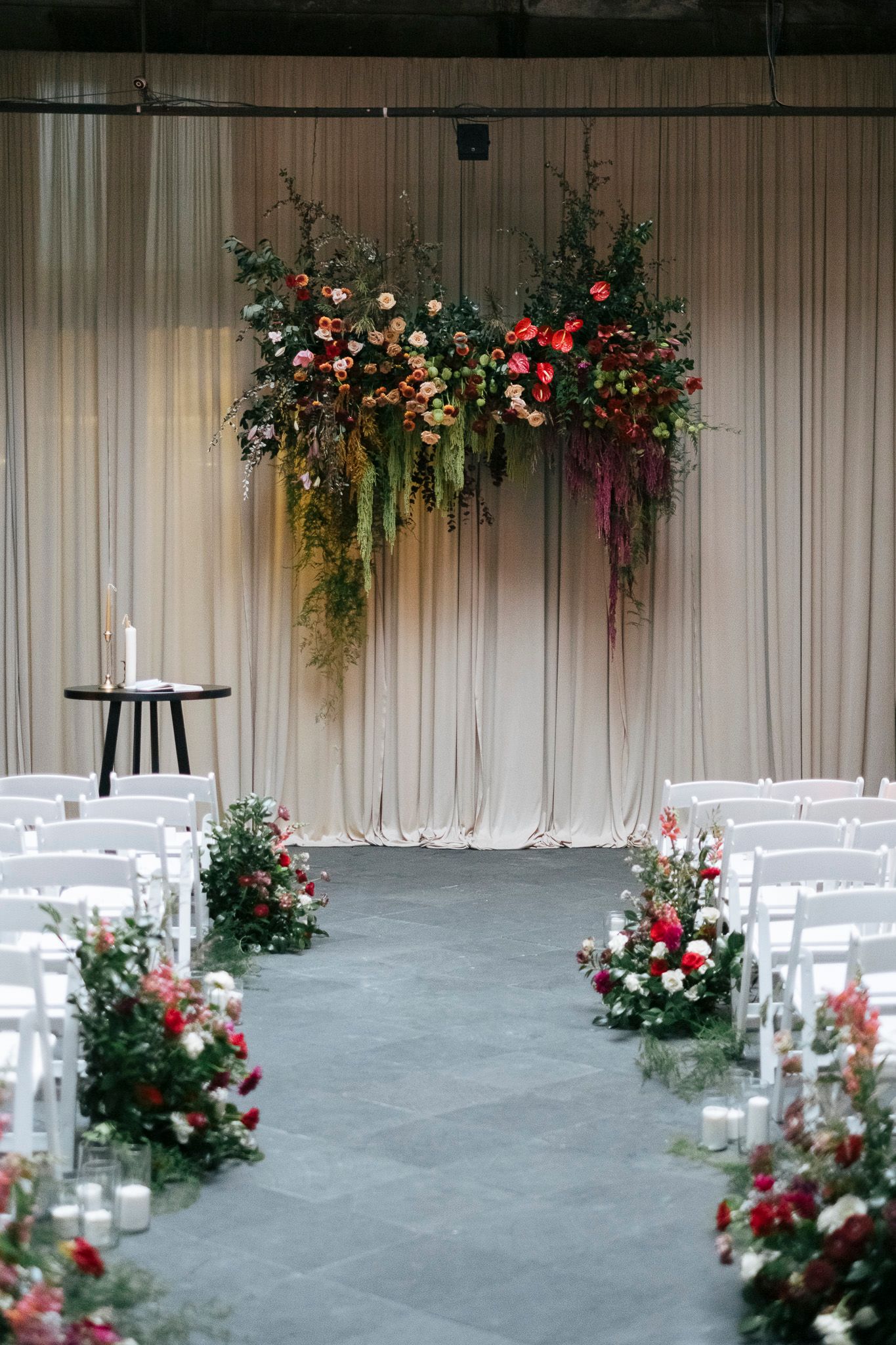 Wedding ceremony setup with white chairs and romantic floral arrangements along the aisle in an elegant indoor venue.
