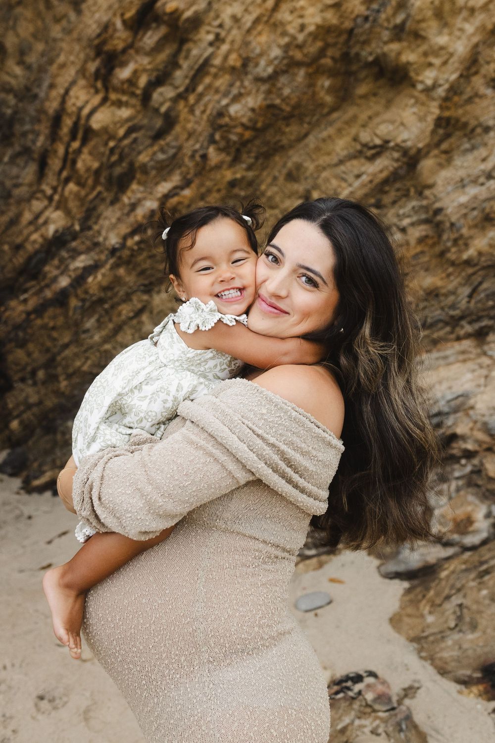 A tender family moment captured against rocky cliffs as a parent and child share an embrace in neutral tones.