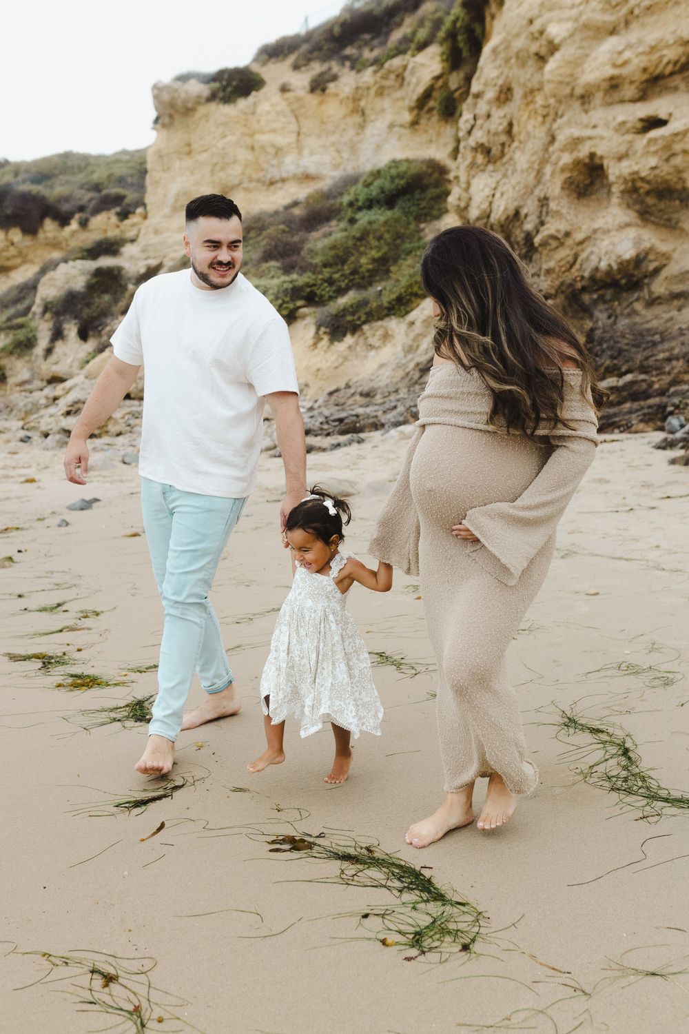 Family walking and playing together on a sandy beach with cliffs in the background.