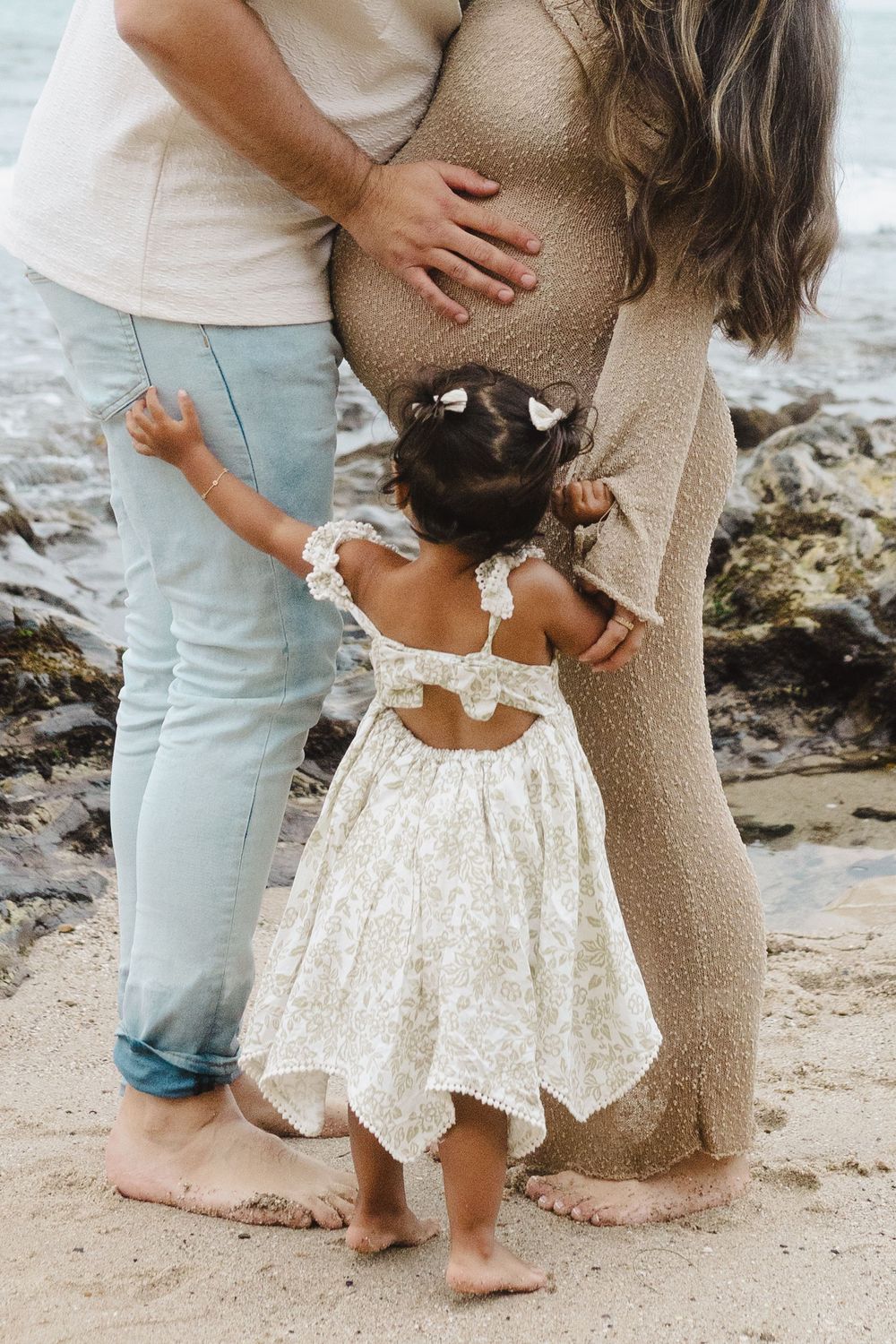Barefoot family members in coordinated beige and white outfits stand together on a beach.