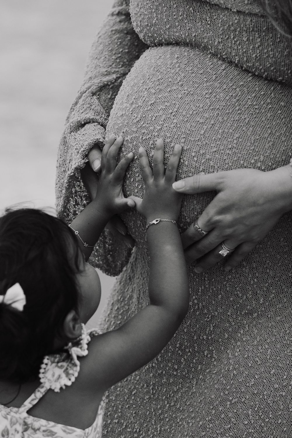Small hands reach up to touch a pregnant belly wrapped in a soft beige sweater.