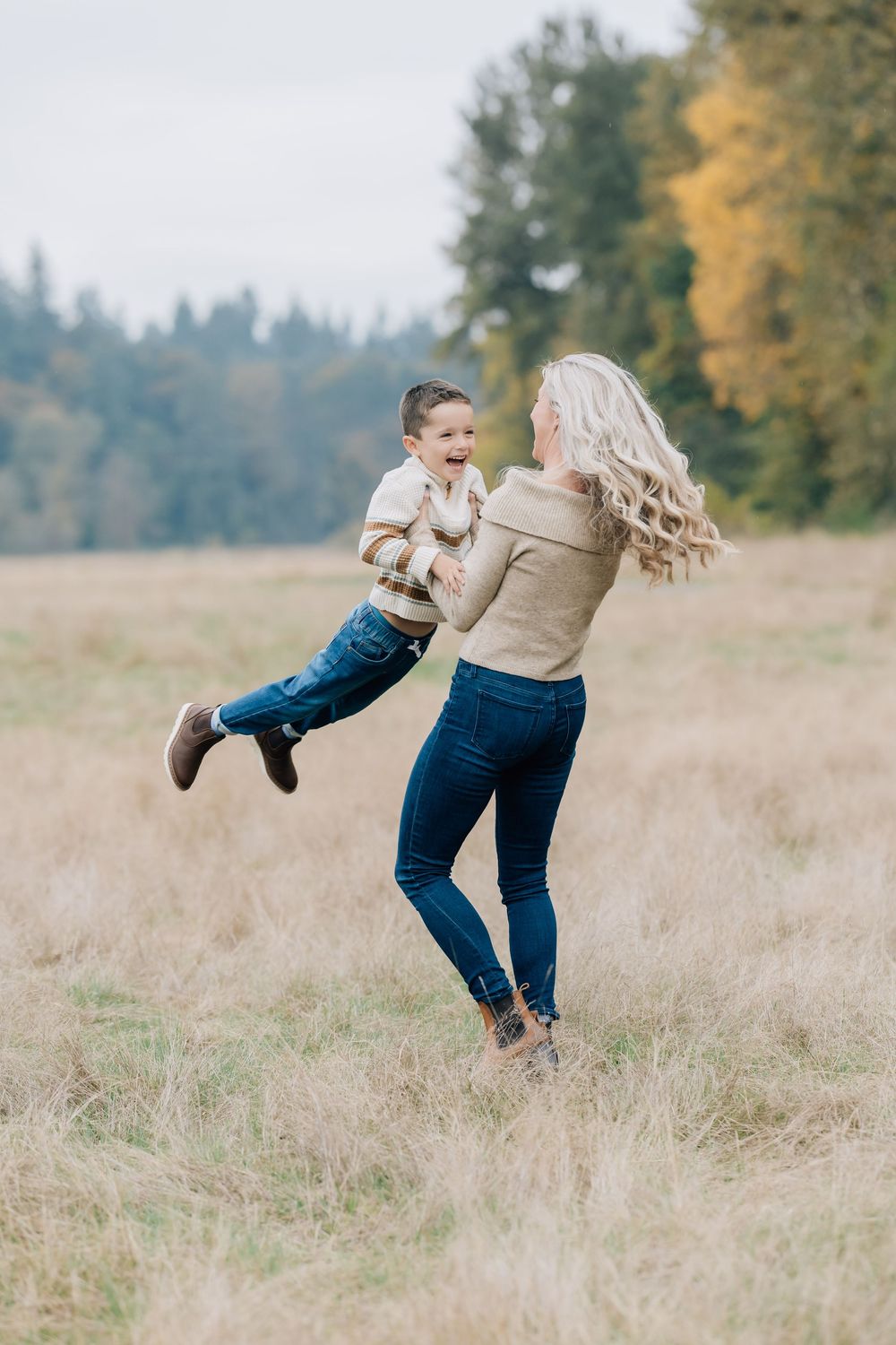 Joyful mother lifting and spinning her laughing son in a golden fall meadow.