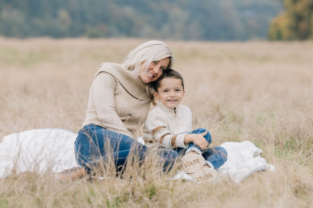 Smiling mother and young son sitting together on a blanket in a fall meadow.