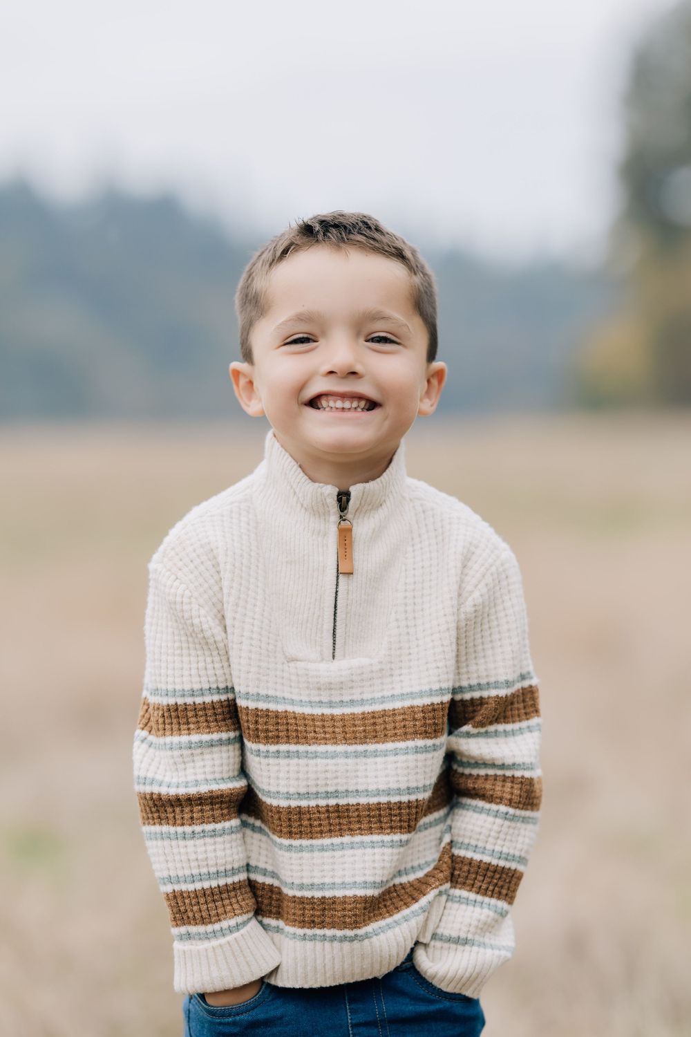 Happy young boy in a striped sweater smiling in an autumn field.