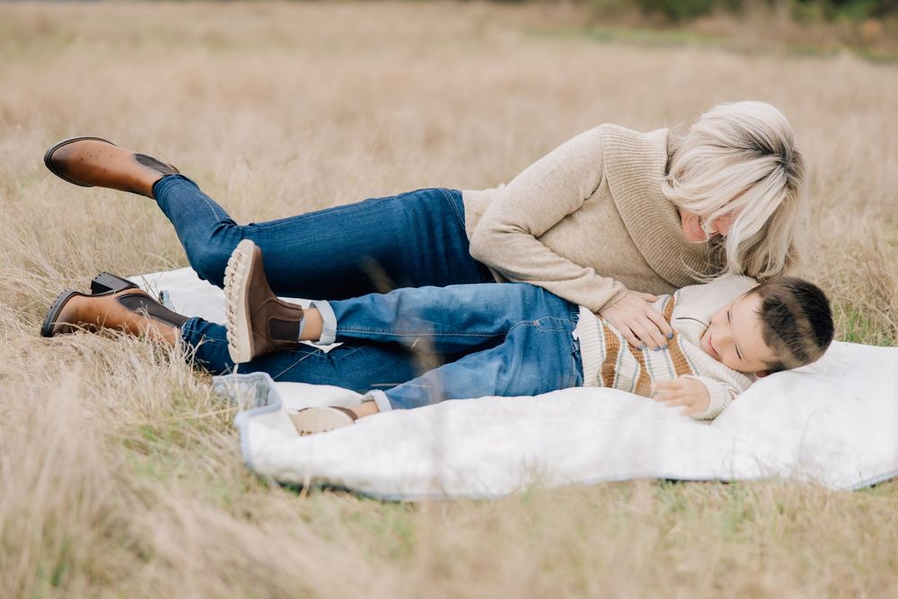 Mother and son cuddling together on a white blanket in a golden meadow.