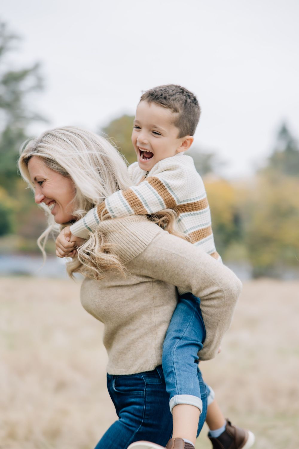 Happy mother giving laughing young boy a piggyback ride in autumn field.
