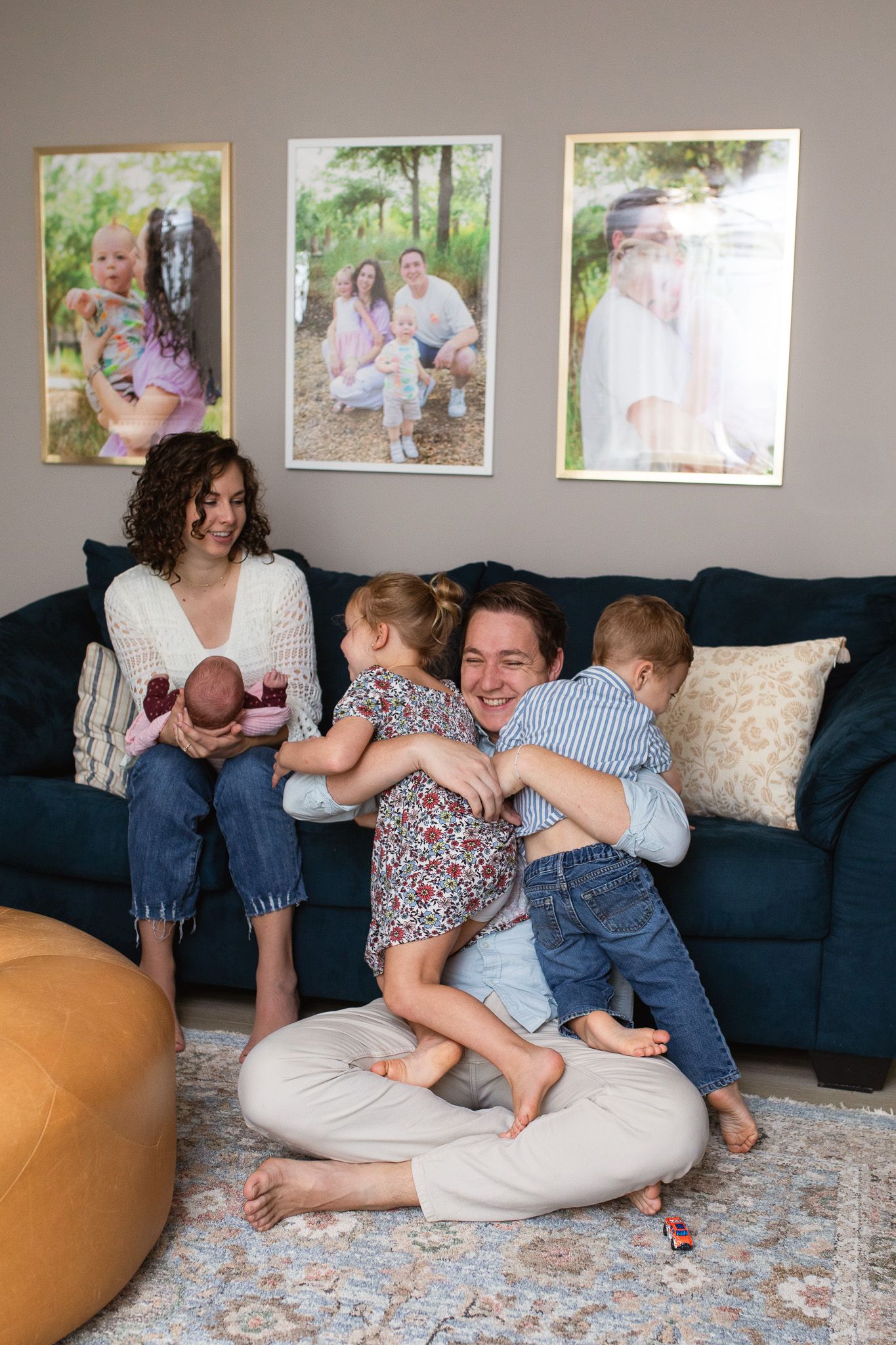 dad and kids hug while mom watches while holding newborn in their living room