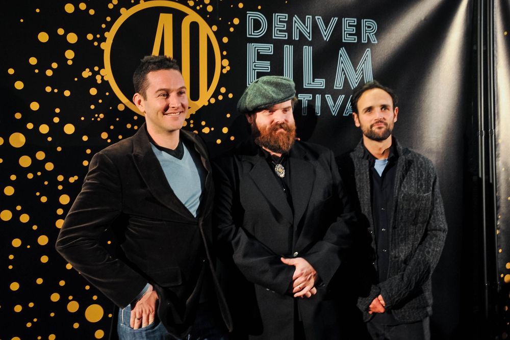 A group poses together at the Denver Film event against a dark background with golden decorative elements.