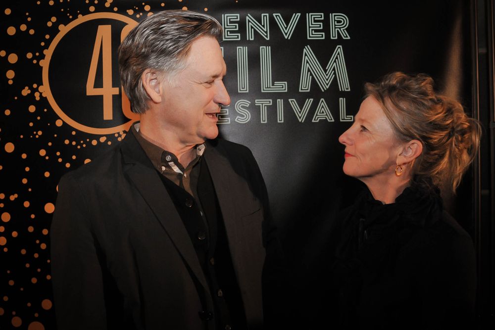 Two people in formal attire converse at an event with the Denver Film Festival logo and lights in the background.