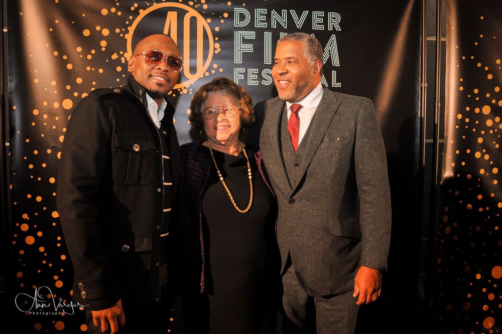 Group of people pose at formal event with sparkling lights and Denver signage in background.