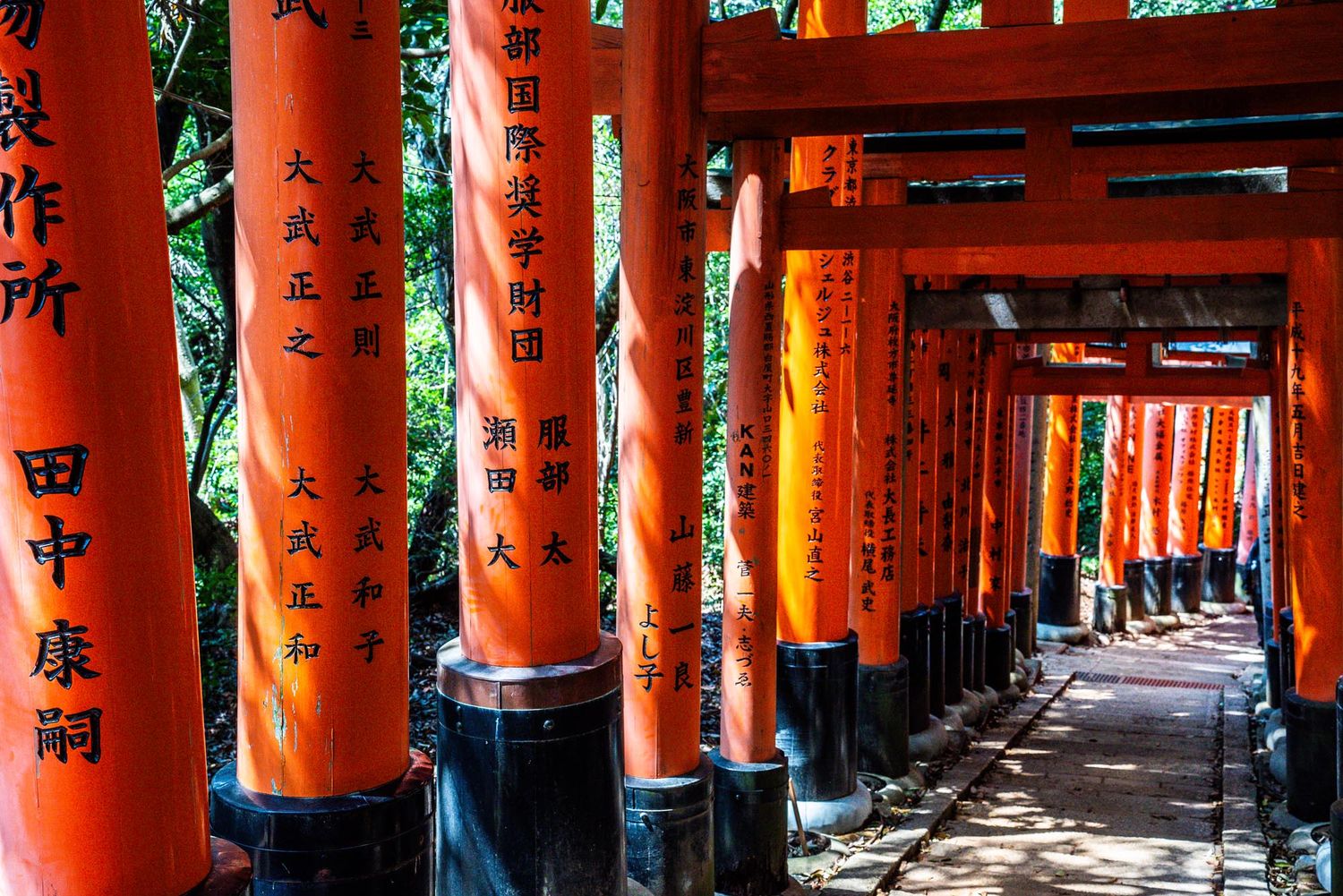 Long corridor of vibrant orange torii gates with Japanese characters at Fushimi Inari Shrine in Kyoto.