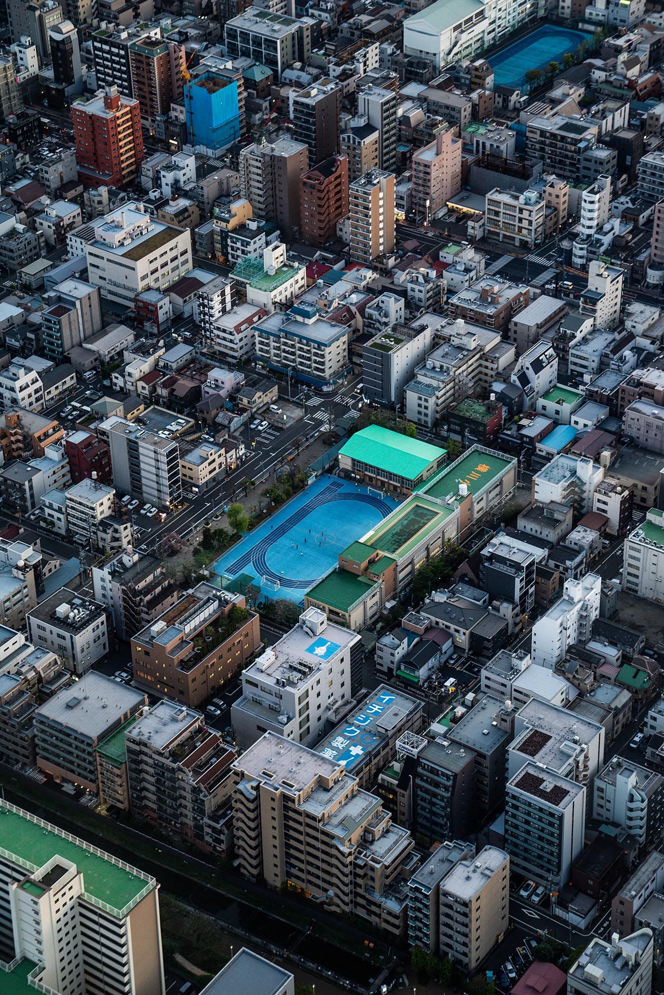 Aerial view of dense urban Tokyo architecture with residential buildings and blue swimming pools scattered throughout.