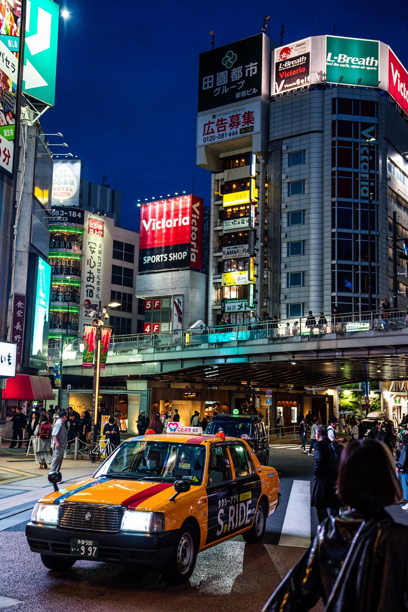 Vibrant nighttime cityscape in Japan with illuminated neon signs, buildings and yellow taxis on a busy street.
