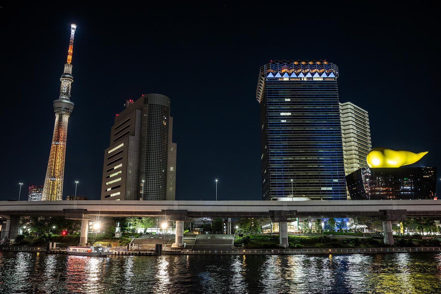 Tokyo Skytree and modern buildings illuminate the night skyline along the Sumida River in Japan.