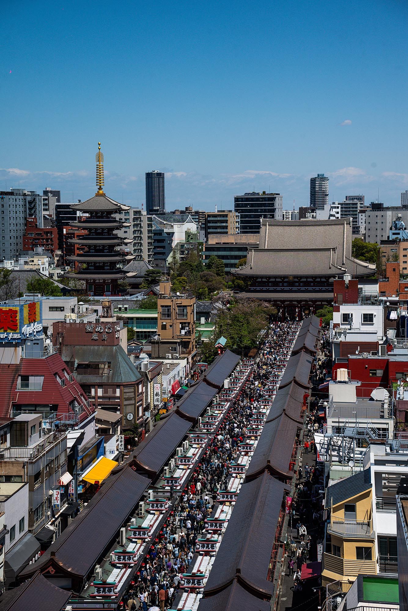 Aerial view of crowded Nakamise shopping street leading to Senso-ji Temple in Asakusa, Tokyo with pagoda and city skyline.