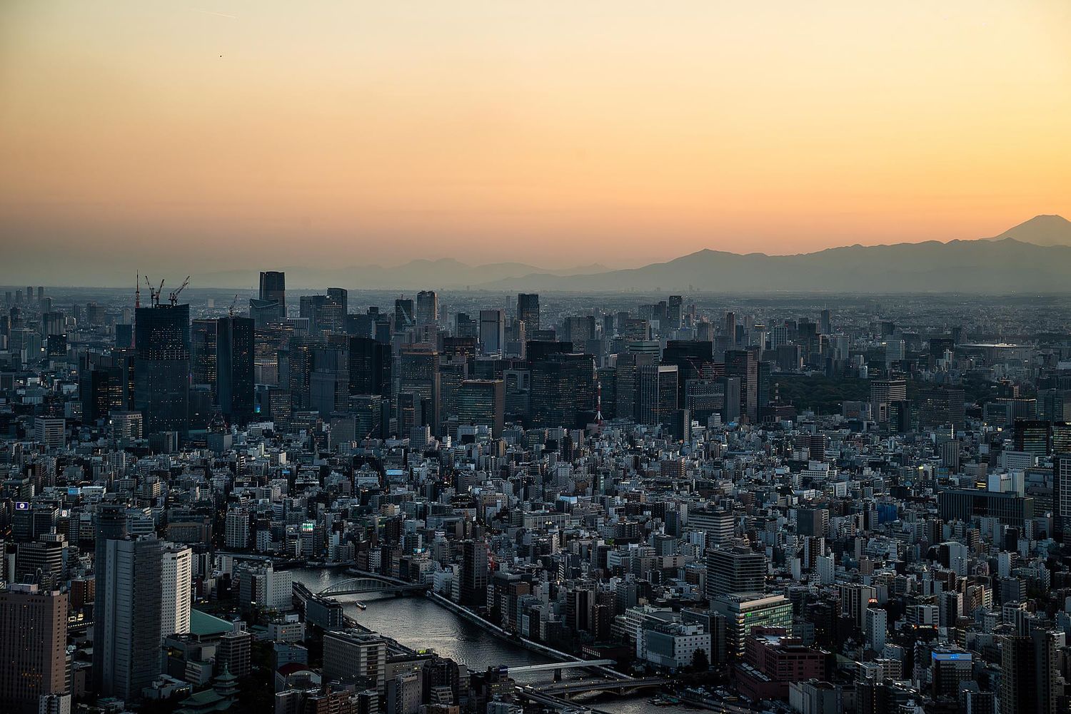 Panoramic aerial view of a dense cityscape with mountains in the background during golden sunset hour.