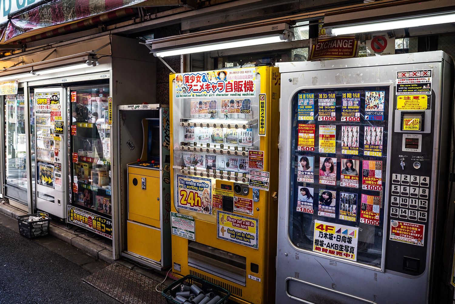 Row of illuminated Japanese vending machines at night selling drinks and snacks along a street.