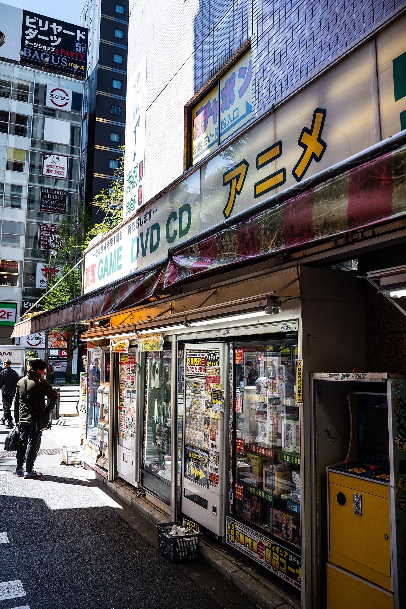 A row of small shops and businesses with Japanese signage along a narrow urban street during daytime.