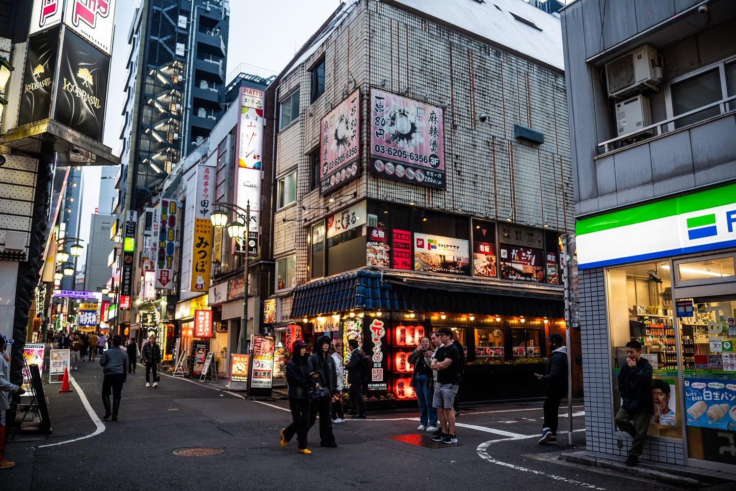 Narrow urban street in Japan with tall buildings, signs, and power lines creating a dense cityscape atmosphere.