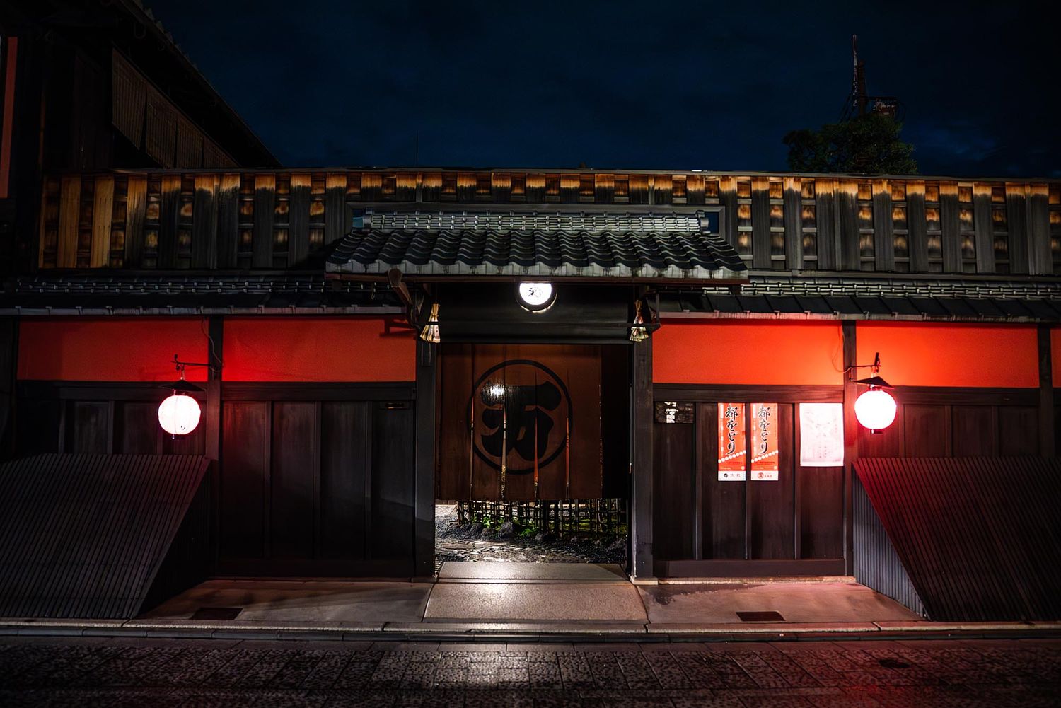 A dark urban street scene at night with red neon lights illuminating storefronts and empty sidewalks.