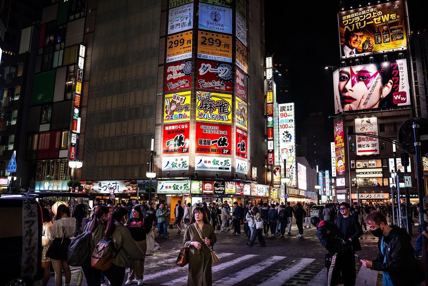 Bustling nighttime street scene in Tokyo's Shibuya district with bright neon signs and illuminated billboards lighting up the crossing.