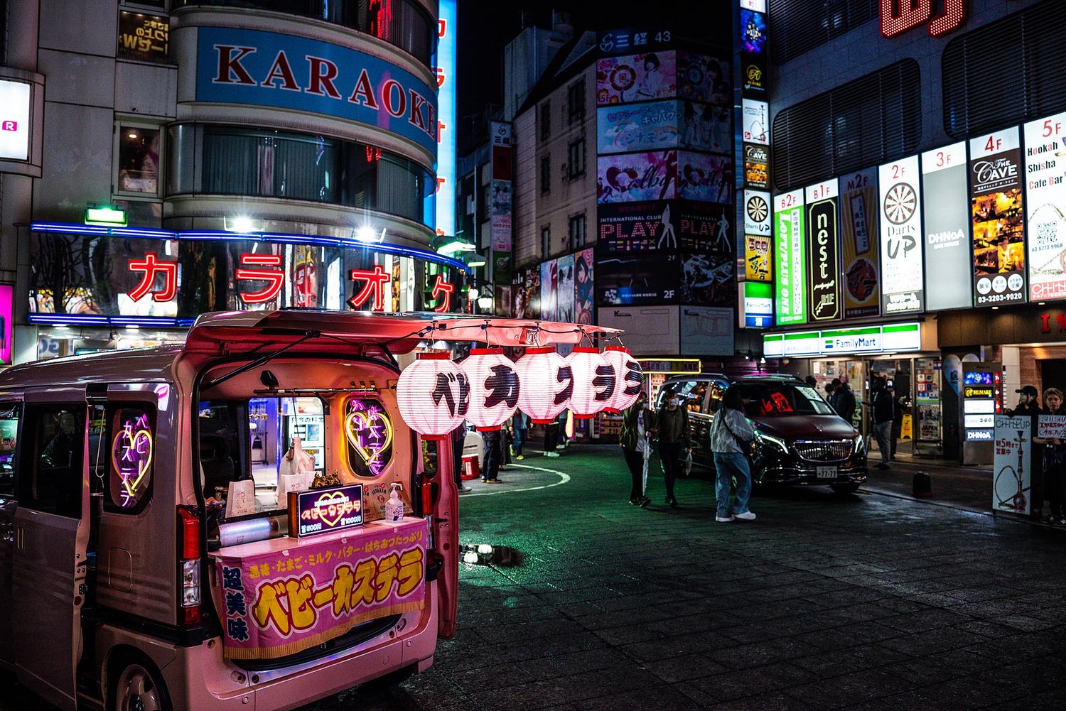 Vibrant neon signs illuminate a busy nighttime street scene in an Asian entertainment district with colorful storefronts.