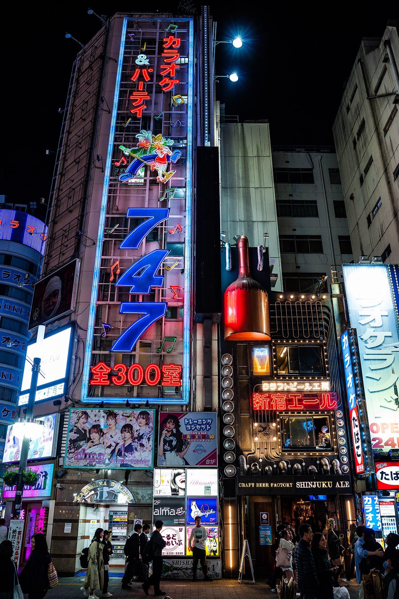 Vibrant neon signs illuminate a busy nighttime street in Tokyo's entertainment district with tall buildings and bright advertisements.