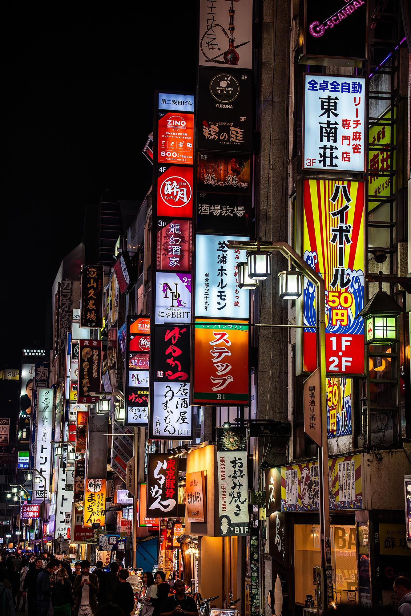 Vibrant neon signs illuminate a bustling Japanese street at night with colorful advertisements and kanji characters.